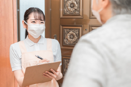 玄関先で体調を聞き取りメモする女性看護師